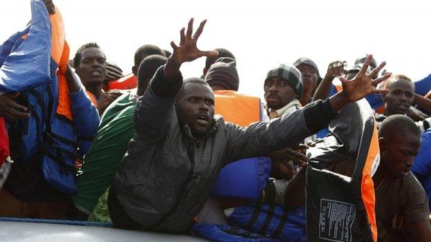 A group of Saharan Africans on board a rubber dinghy reach out for life jackets tossed to them by rescuers of the NGO Migrant Offshore Aid Station (MOAS) some 25 miles off the Libyan coast