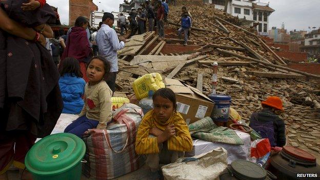 People sitting with their belongings outside a damaged building in Kathmandu.