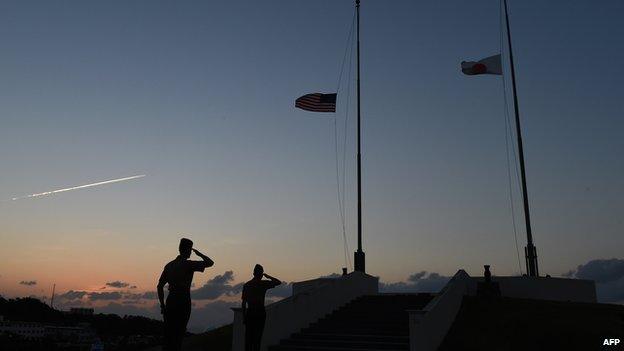 Servicemen of US Marine Corps salute while Japanese (R) and US flags are being taken down at the evening colors ceremony at the Camp Foster near Futenma Base in Ginowan, Okinawa prefecture, on November 14, 2014.