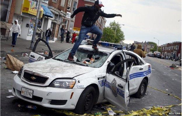 Demonstrators jump on a damaged Baltimore police department vehicle