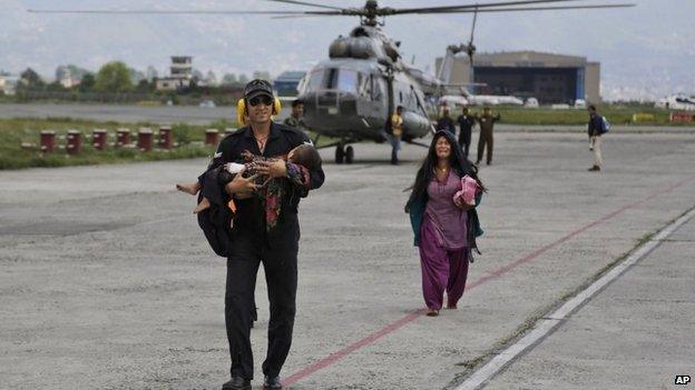 An Indian Air Force person walks carrying a Nepalese child, wounded in Saturday’s earthquake, to a waiting ambulance as the mother follows after they were evacuated from a remote area at the airport in Kathmandu, Nepal, Monday, April 27, 2015