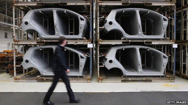 A Volkswagen employee walks past stacked stamped car body parts