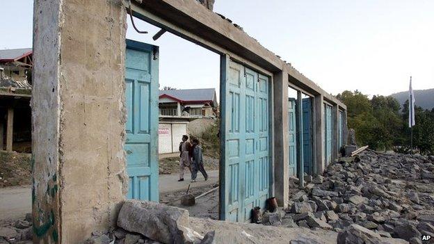 Kashmiris walk past the remains of shops destroyed by an earthquake in Pakistan on 8 October 2005