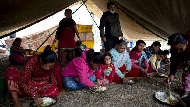 Nepalese people eating a meal in a makeshift tent after the earthquake there.