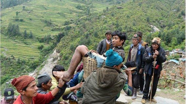 villagers carry an injured youth in a basket down the hillside to an Indian Army helicopter at Uiya village, in northern-central Gorkha district in Nepal