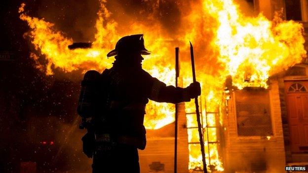 A Baltimore fire-fighter attacks a fire at a convenience store and residence during clashes after the funeral of Freddie Gray in Baltimore, Maryland in the early morning hours 28 April 2015