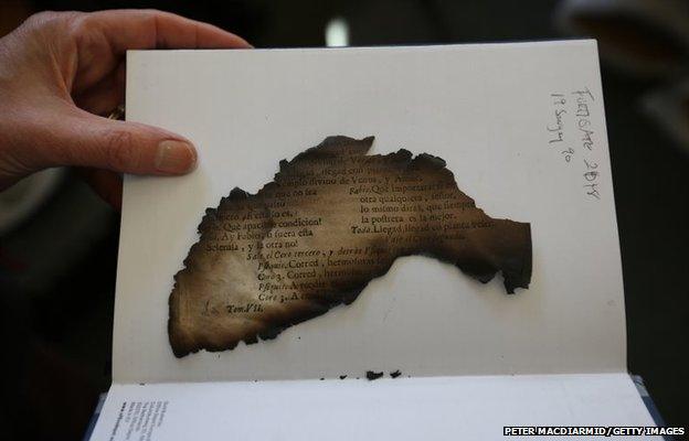 A burnt fragment of an antique book rescued from Clandon Park House is displayed by a conservator