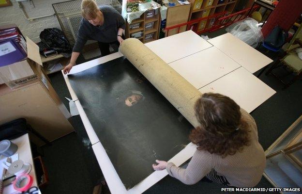 National Trust conservators unroll an 18th century painting rescued from Clandon Park House