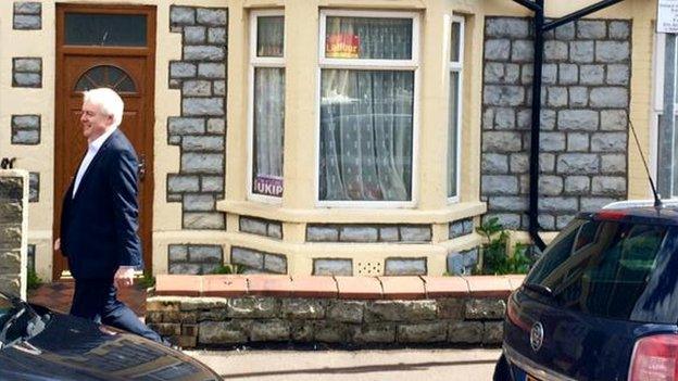 Carwyn Jones passing a house with Labour and UKIP posters in the window