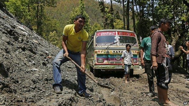 Bus driver digs mud from road in the Gorkha District of Nepal. 30 Apr 2015