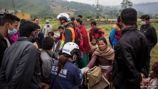 People crowd around a small table giving medical checks and tending to minor injuries by medical staff from a China search and rescue team in a field on the side of the road on 30 April, 2015 in Kathmandu, Nepal