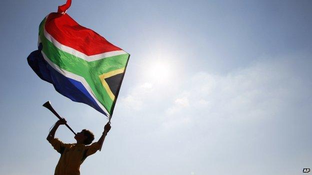 A supporter (in silhouette) waves a South African flag as he blows a vuvuzela, prior to the World Cup group A soccer match between South Africa and Mexico at Soccer City in Johannesburg, South Africa, on 11 June 2010