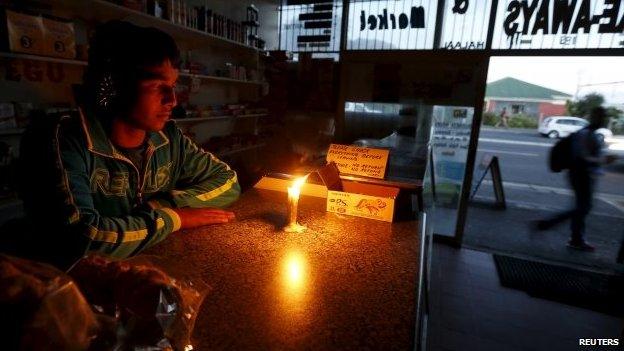 A shopkeeper waits for customers in his candlelit fast food store during a load shedding electricity blackout in Cape Town in South Africa, 15 April 2015