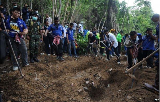 This picture taken on May 2, 2015 shows rescue workers and forensic officials digging out skeletons from shallow graves covered by bamboo at the site of a mass grave at an abandoned jungle camp in the Sadao district of Thailand's southern Songkhla province bordering Malaysia