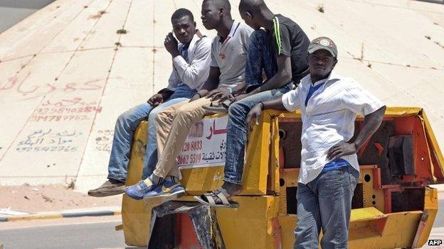 African immigrants sit on a power generator in a street close to a main bridge in central Tripoli, the Libyan capital, as they wait for job offers, on 11 May 2015