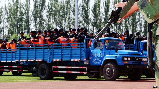 This picture taken on 27 May 2014 shows security forces standing behind the accused wearing orange vests on trucks during a mass sentencing in Ili prefecture, northwest China's Xinjiang region.