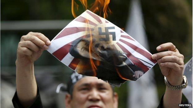 An anti-Japan activist burns a poster depicting Japanese Prime Minister Shinzo Abe with a swastika on a rising-sun flag during an anti-Japan rally in front of the Japanese embassy in Seoul, South Korea, 28 April 2015