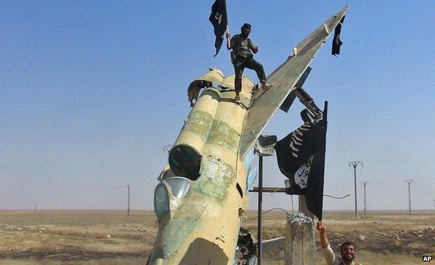 Islamic State fighters wave the group's flag near a Syrian fighter jet in Raqqa in Syria, undated