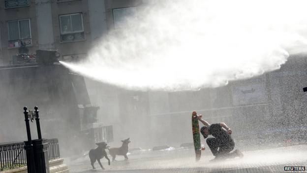 A protester kneels with his skateboard amidst water jets during a demonstration to demand changes in the education system at Santiago