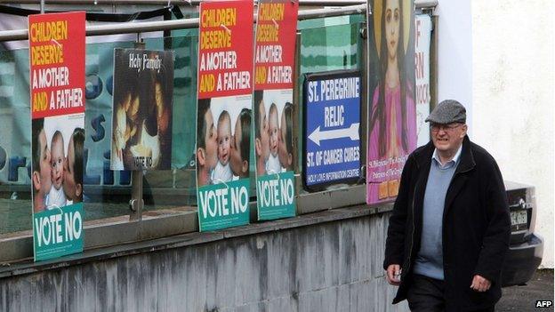 A man walks past a row of anti same-sex Vote No posters in Knock, Ireland