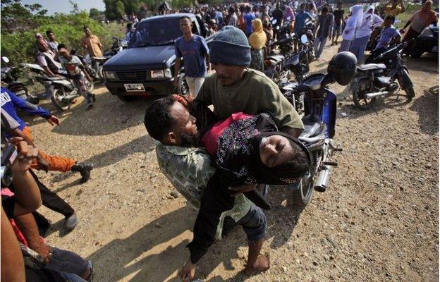 Acehnese men help an unconscious migrant woman upon her arrival in Simpang Tiga, Aceh province, Indonesia Wednesday, May 20, 2015.