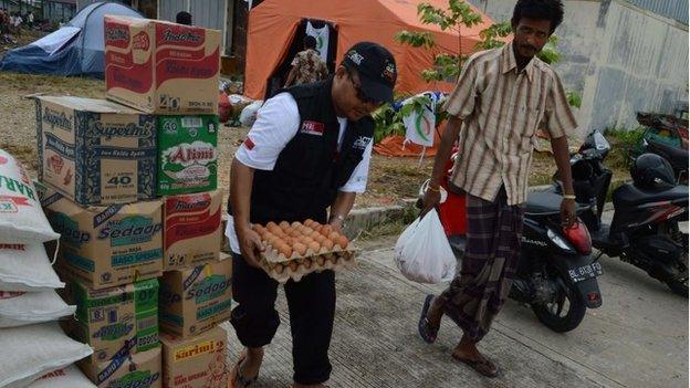 In this photograph taken on May 18, 2015 an Indonesian volunteer (L) and a rescued migrant Rohingya migrant from Myanmar carry donated food supply at a warehouse facility converted into quarters in the fishing port of Langsa in Aceh province.