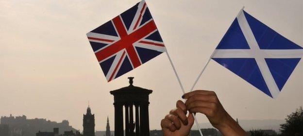 Saltire and Union Jack held up in front of the Edinburgh skyline