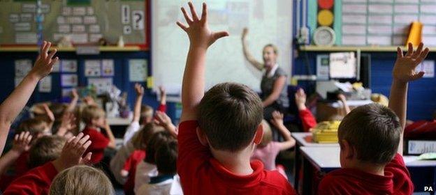 Rear view of primary school children raising their hands in a classroom