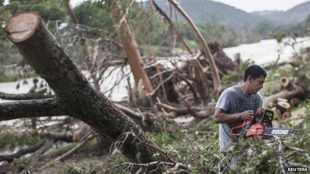 A man uses a chainsaw to cut fallen tree trunks into small pieces along the banks of the Blanco River in Wimberley, Texas (26 May 2015)