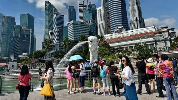 Tourists visit Singapore's famous Merlion (C) in front of the skyline of the city's financial business district on 25 February 2015