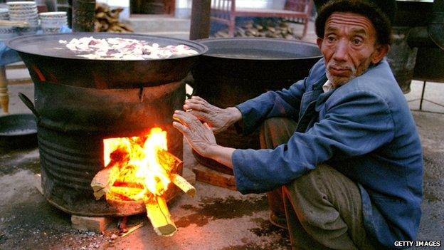 A Muslim Uighur man warms himself while cooking mutton stew early in the morning at a market April, 28 2002 in Kashgar, Xinjiang Region, China