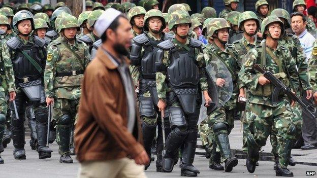 Armed Chinese soldiers march on patrol as a Uighur man crosses the street in Urumqi on July 15, 2009 in northwest China's Xinjiang province