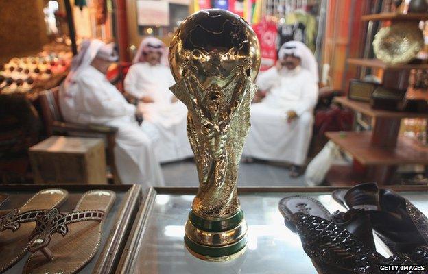 Arab men sit at a shoemaker's stall with a replica of the FIFA World Cup trophy in the Souq Waqif traditional market 24 October 2011