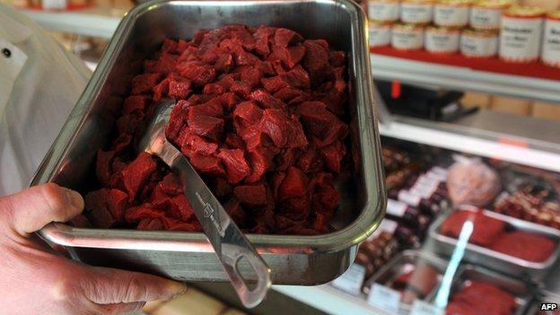 A man holding a tray of horsemeat in front of a butcher's counter