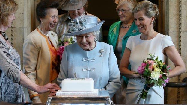 Sophie, Countess of Wessex, and Princess Anne, Princess Royal, look on as Queen Elizabeth II cuts a Women's Institute cake