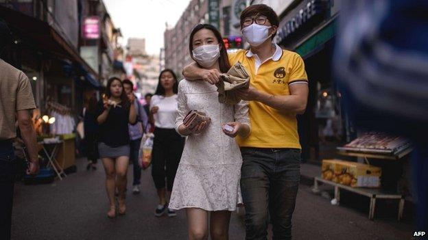 A couple wearing face masks walk on a street in the Hongdae area of Seoul - 7 June 2015