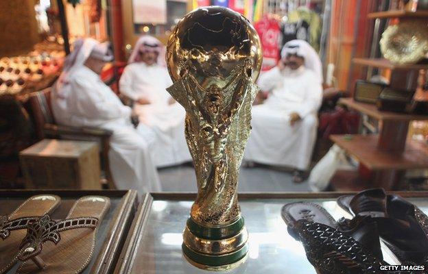 Arab men sit at a shoemaker's stall with a replica of the FIFA World Cup trophy in the Souq Waqif traditional market 24 October 2011