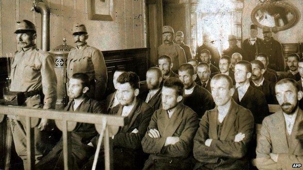 An archive photo of Gavrilo Princip and his co-accused on trial in a courtroom, flanked by guards