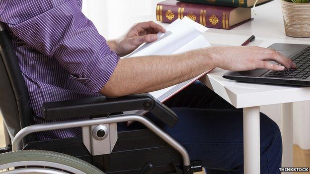 a man in a wheelchair sitting at a desk with a laptop