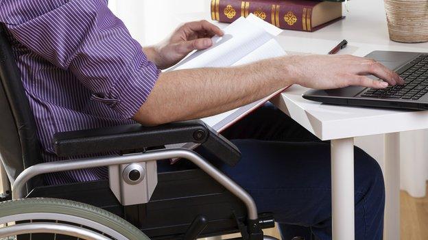 a man in a wheelchair sitting at a desk with a laptop