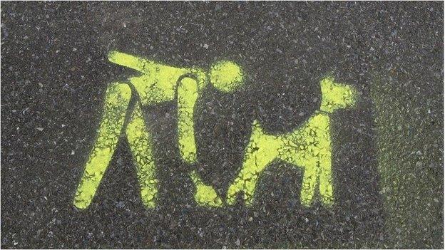 A painted pavement sign telling dog owners to clean up after their animals