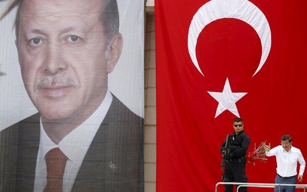 Turkey's Prime Minister Ahmet Davutoglu throws carnations to his supporters as he stands in front of a portrait of President Tayyip Erdogan and a national flag during an election rally on 3 June 2015