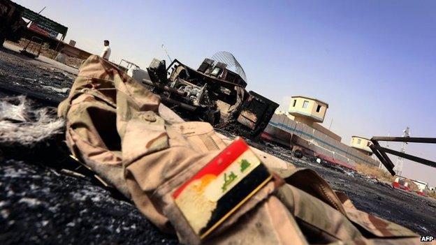 Abandoned Iraqi army uniform lies on the ground in front of a burnt-out military vehicle in Mosul (11 June 2014)