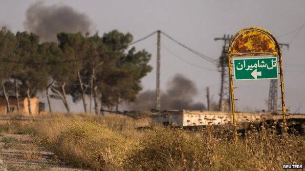 Smoke rises in the distance behind a road sign from the Assyrian village of Tel Nasri, northern Syria (21 May 2015)