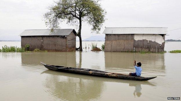 A schoolboy rows his boat past partially submerged huts in the Morigaon district of Assam