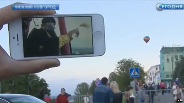 An observer watches the live feed of the blessing on his phone as the balloon drifts away in the background