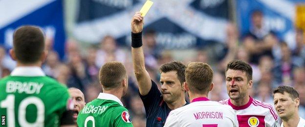 Italian referee Nicola Rizzoli shows James McCarthy a yellow card for elbowing Russell Martin in an aerial challenge