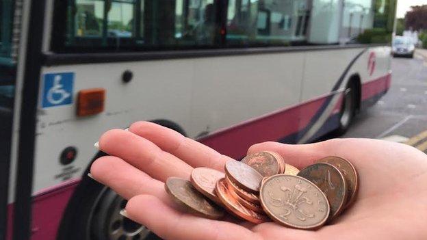 Hand holding coins at a bus stop