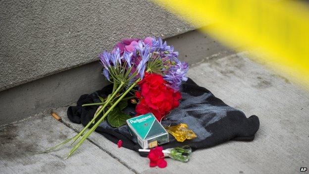 Flowers and a cigarette box form a makeshift memorial