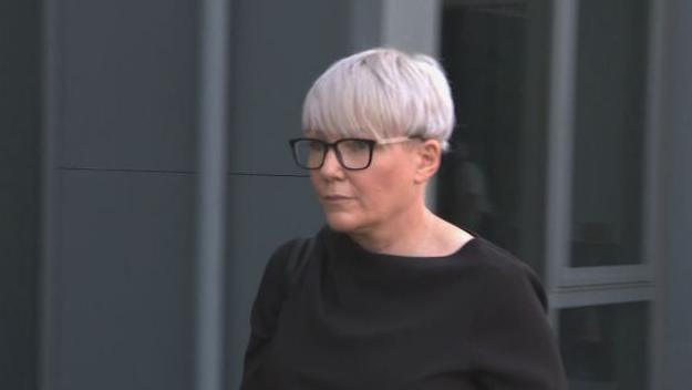 A woman with glasses and short silver hair walking outside a building